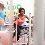 Woman lunging on sled in gym next to man using cable machine