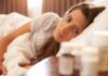 Insomnia Fix That Slows Cellular Aging Woman lying in bed looking at pill bottles on a bedside table