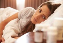 Insomnia Fix That Slows Cellular Aging Woman lying in bed looking at pill bottles on a bedside table