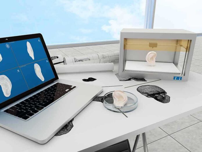 3D printer and laptop creating a model ear on a lab desk