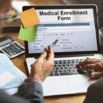 Laptop displaying a medical enrollment form with two people reviewing it