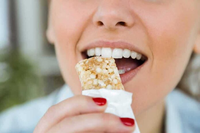 shutterstock_564161623 Person taking a bite of a granola bar