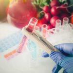 Gloved hand holding test tubes near fresh vegetables