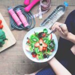 Best Protein For Building Muscle person eating a fresh fruit and veggie salad with workout gear