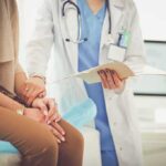 The Urination Habit That Could Be Messing Up Your Bladder Doctor comforting patient while reviewing medical chart