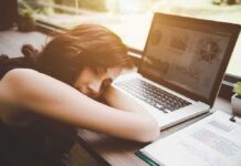 Woman resting her head on desk beside an open laptop