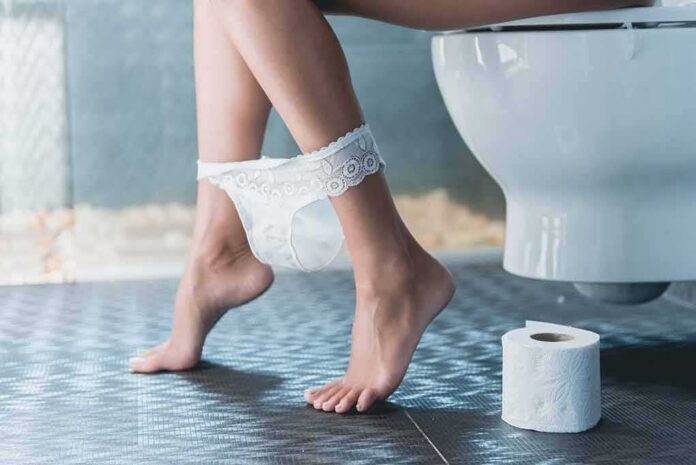 Person sitting on a toilet with underwear at ankles and toilet paper nearby