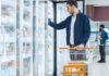Man with shopping cart opens freezer door in grocery store