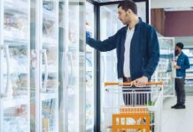 Man with shopping cart opens freezer door in grocery store