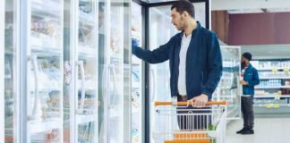 Man with shopping cart opens freezer door in grocery store