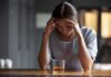 Woman with head in hands at a bar with a glass of whiskey