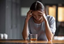 Woman with head in hands at a bar with a glass of whiskey
