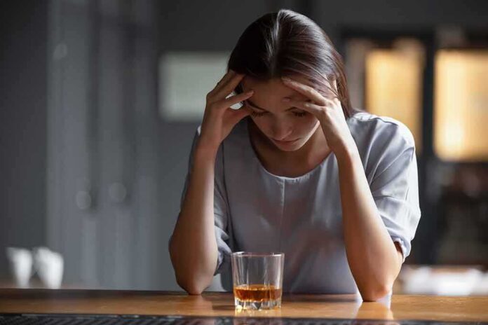 Woman with head in hands at a bar with a glass of whiskey