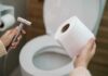 Hands holding a bidet sprayer and toilet paper near an open toilet