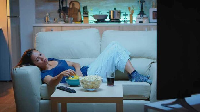 shutterstock_1839714829 Woman lounging on a sofa watching TV at night
