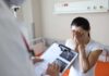 Woman covering her face while doctor holds a clipboard in a hospital room