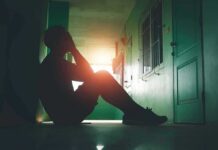 Person sitting on hallway floor with head in hands at sunset