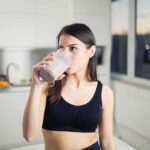 Woman in sportswear drinking a smoothie in a kitchen