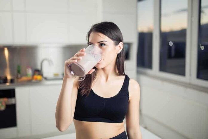 Woman in sportswear drinking a smoothie in a kitchen