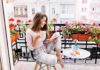 Woman on balcony with coffee and tablet among pink flowers
