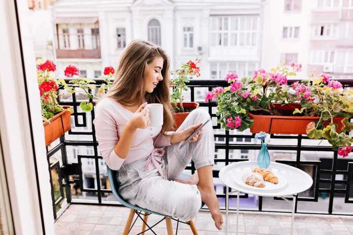 Woman on balcony with coffee and tablet among pink flowers
