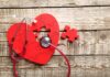 Red heart puzzle with stethoscope on wooden surface