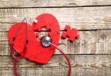 Red heart puzzle with stethoscope on wooden surface