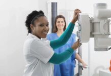 Radiologic technologist adjusting X-ray machine with patient standing behind