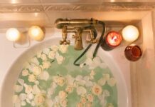 Bathtub filled with water and white roses under candles